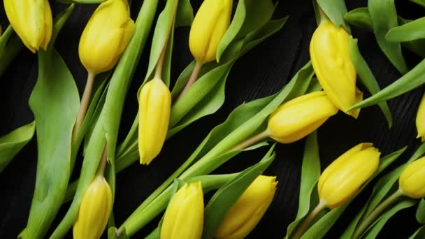 Hermosos tulipanes amarillos sobre fondo de madera rústico negro. Vista superior — Vídeo de stock