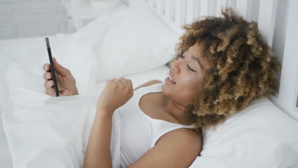 Усміхнена жінка розслабляється з телефоном у ліжку — стокове відео