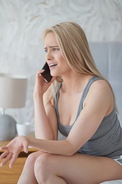 Mellersta år blond kvinna sitter i hennes hem sängen och argumentera med någon — Stockfoto