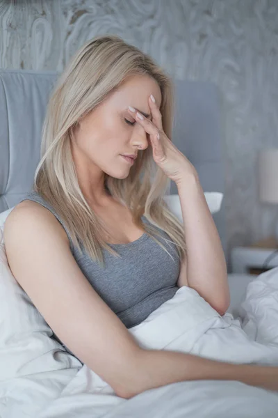 Women sitting on bed holding her head. She has a painful headache — Stock Photo, Image