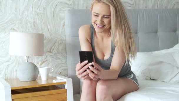 Nette Frau mittleren Alters, die morgens auf ihrem Bett sitzt und ihr Smartphone checkt — Stockvideo