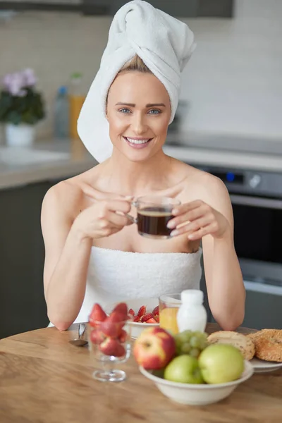 Όμορφη γυναίκα με πετσέτα στο κεφάλι έχοντας ένα υγιεινό πρωινό και καφές — Φωτογραφία Αρχείου