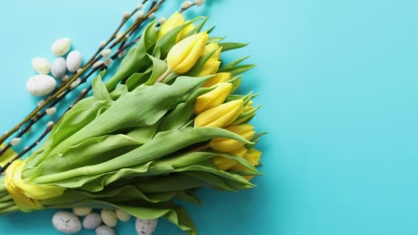 Праздничные украшения с пасхальными яйцами и желтыми тюльпанами над синим — стоковое видео