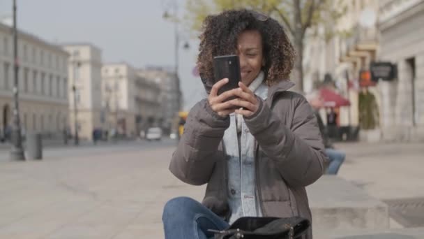 Vacker flicka med afro frisyr sitter på bänken på stads gatan — Stockvideo