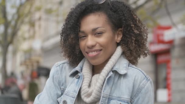 Bedårande flicka med afro frisyr sitter på bänken på stads gatan — Stockvideo