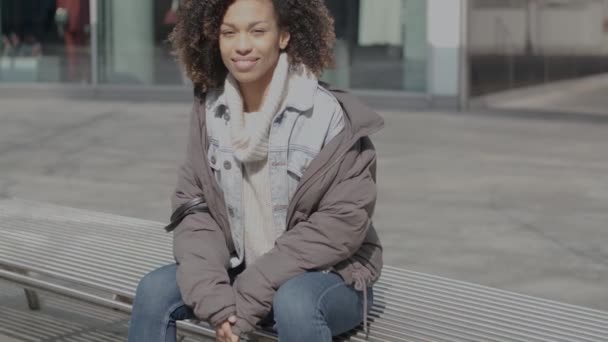 Hermosa chica con corte de pelo afro sentado en el banco en la calle de la ciudad — Vídeos de Stock