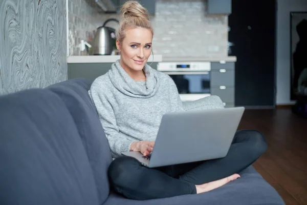 Middle aged woman sitting on sofa in her living room and working on laptop — Stock Photo, Image