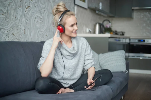 Schattige middelbare leeftijd blonde vrouw zittend op de sofa in haar huis en luister naar de muziek — Stockfoto