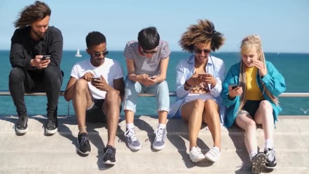 Diversos amigos contemporáneos con smartphones en primera línea de mar — Vídeos de Stock