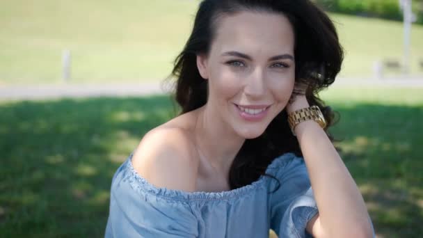 Портрет привабливої брюнетки в блакитній сукні, що сидить у парку — стокове відео