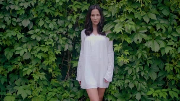 Ženská modelka v bílém tuniku se zelenými listy na pozadí — Stock video