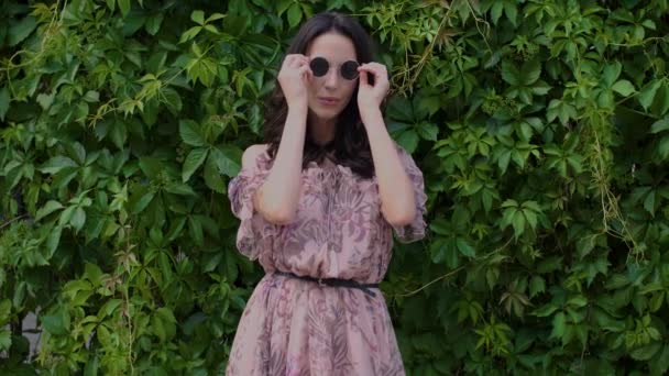 Stijlvolle hipster meisje poseren over groene bladeren Bush achtergrond — Stockvideo