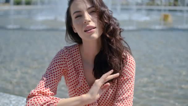 Портрет красивої дівчини в барвистому літньому одязі, що сидить біля фонтану — стокове відео