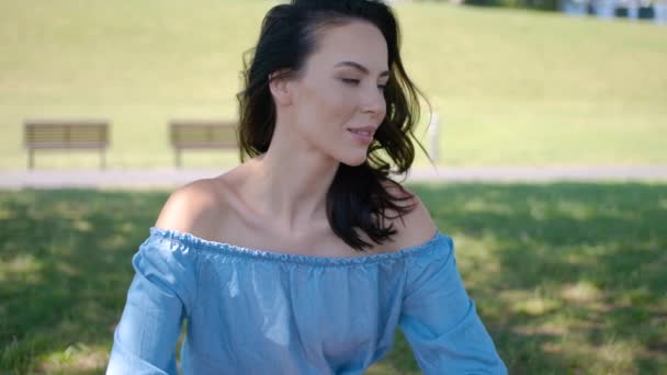Πορτραίτο της ελκυστική μελαχρινή γυναίκα με μπλε φόρεμα κάθεται σε ένα πάρκο — Αρχείο Βίντεο
