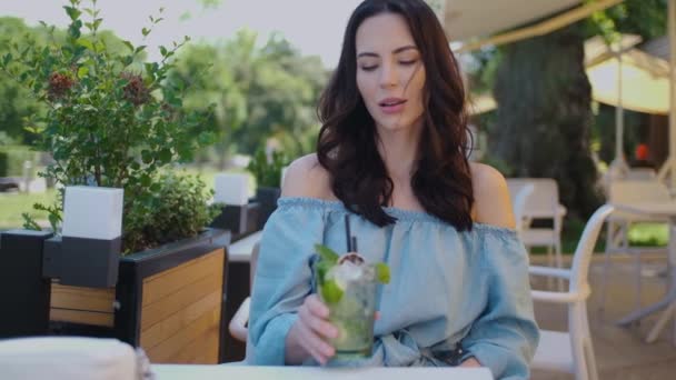 Богіфул жінка сидить у відкритому ресторані і ковток мохіто свердлить в літній спекотний день — стокове відео
