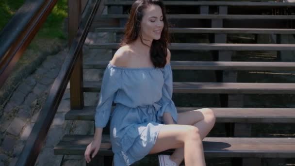 Schattige brunette vrouw zittend op trappen in de buitenlucht — Stockvideo