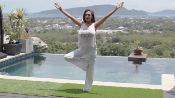 Mujer tranquila practicando yoga junto a la piscina contra el hermoso paisaje de la orilla del mar — Vídeos de Stock