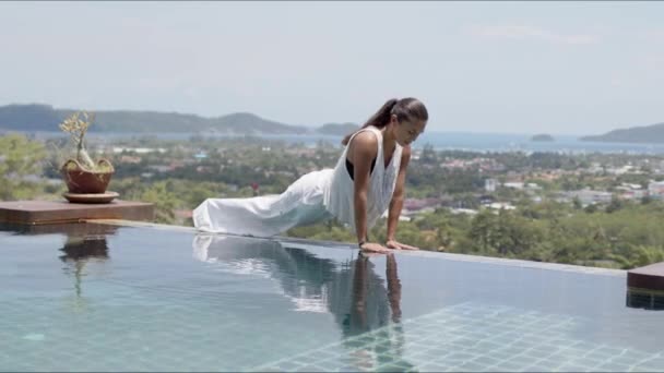 Mulher relaxada fazendo exercício de cobra de bebê perto da piscina contra belas paisagens — Vídeo de Stock