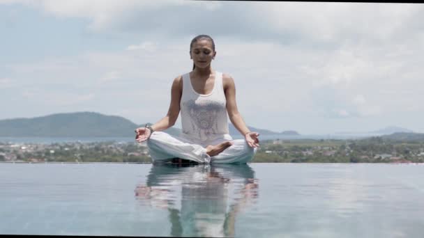 Gelassene Frau praktiziert Yoga in Lotusstellung am Pool gegen den Himmel — Stockvideo
