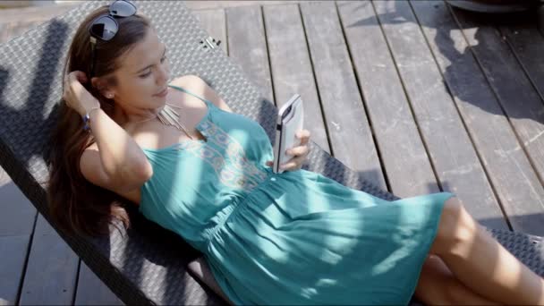 Mujer en vestido azul descansando en silla de salón y usando teléfono inteligente — Vídeos de Stock