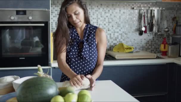 Mulher sorridente em pé no balcão com produtos e amassar massa na cozinha — Vídeo de Stock