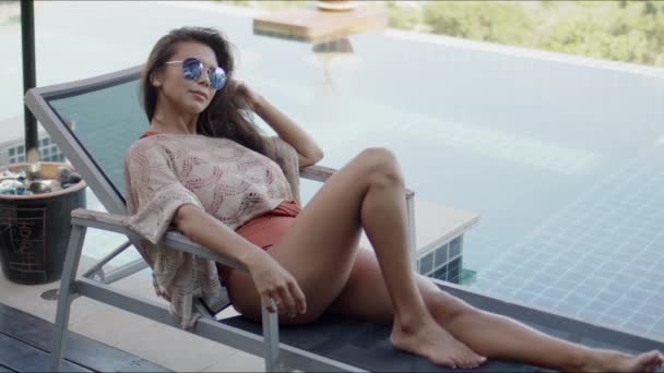 Женщина отдыхает на шезлонге у бассейна, наслаждаясь отдыхом — стоковое видео