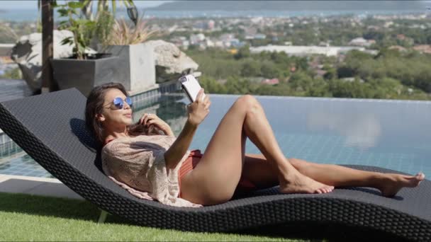 Lounging kvinna tar selfie vid poolen på toppen av hotellet — Stockvideo