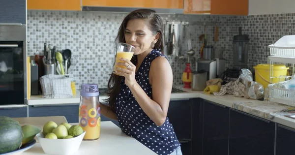 Charming happy woman sipping fresh orange juice standing in kitchen — Stock Photo, Image