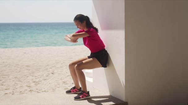 Jeune femme faisant squats muraux sur la plage — Video