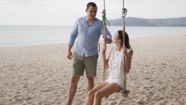 Man teetering woman on swing at lonely coastline — Stock Video