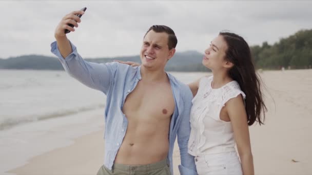 Nöjda människor i kärlek gör selfie på smartphone och ler mot exotiska havet sida — Stockvideo