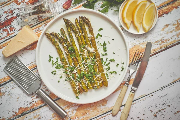 Deliciosos espárragos asados servidos en plato de cerámica blanca. Con queso parmesano, perejil y limón . —  Fotos de Stock