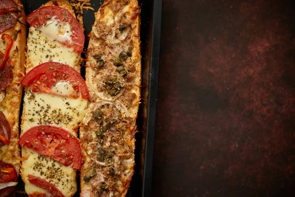 Sanduíches de pizza de baguetes longas com atum, cogumelos, tomates e queijo em uma bandeja de cozedura metálica — Fotografia de Stock