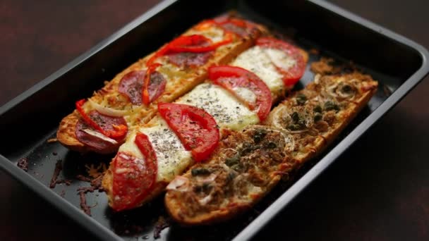 Sanduíches de pizza de baguetes longas com atum, cogumelos, tomates e queijo em uma bandeja de cozedura metálica — Vídeo de Stock