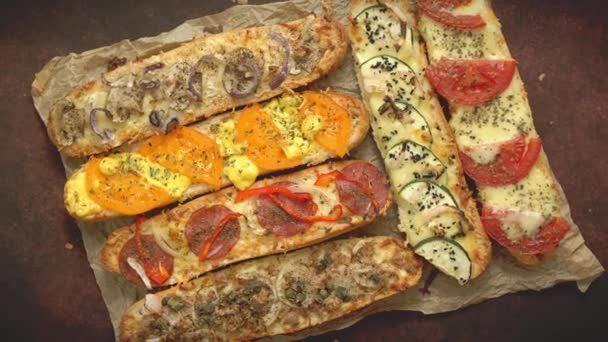 Assortiment van diverse toppings gebakken broodjes. Met gesmolten kaas, groenten, tonijn, olijven en specerijen — Stockvideo
