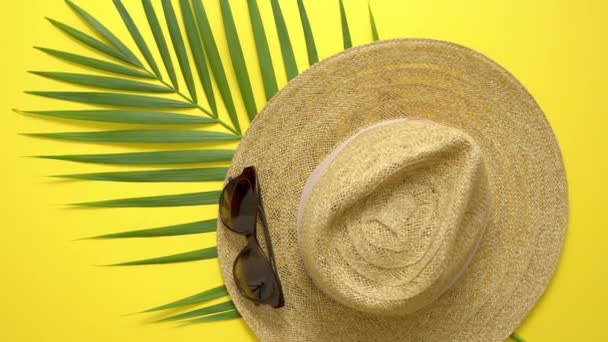 Strohhut, grünes Palmblatt und Sonnenbrille vor gelbem Hintergrund. Sommerkonzept. Flache Lage, Draufsicht — Stockvideo