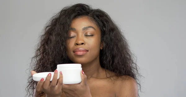 Mujer negra oliendo crema con los ojos cerrados — Foto de Stock