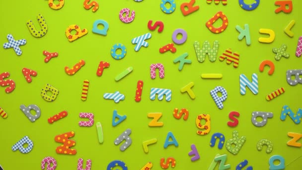 Letras coloridas do alfabeto magnético, plástico e papel colocadas aleatoriamente sobre fundo verde — Vídeo de Stock