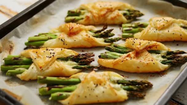 Espárragos verdes al horno en hojaldre espolvoreado con semillas de sésamo. Colocado en un papel de hornear blanco — Vídeos de Stock