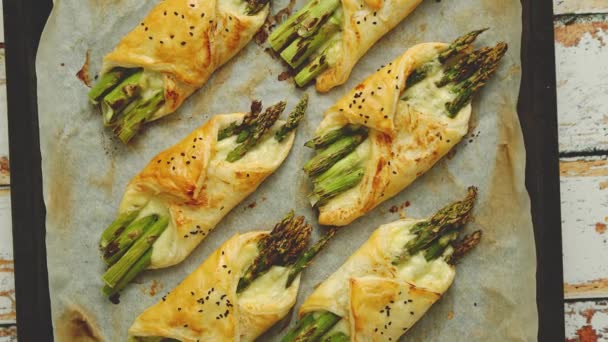 Baked green asparagus in puff pastry sprinkled with sesame seeds. Placed on a white baking paper — Stock Video