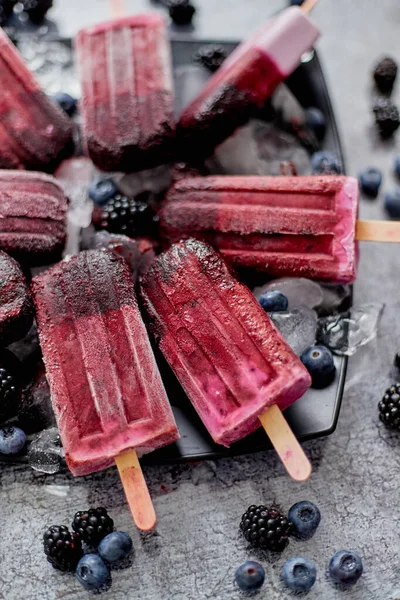 Paletas caseras frescas congeladas de arándanos y moras en un plato negro con hielo sentado en piedra — Foto de Stock