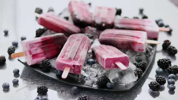 Paletas caseras frescas congeladas de arándanos y moras en un plato negro con hielo sentado en piedra — Vídeo de stock