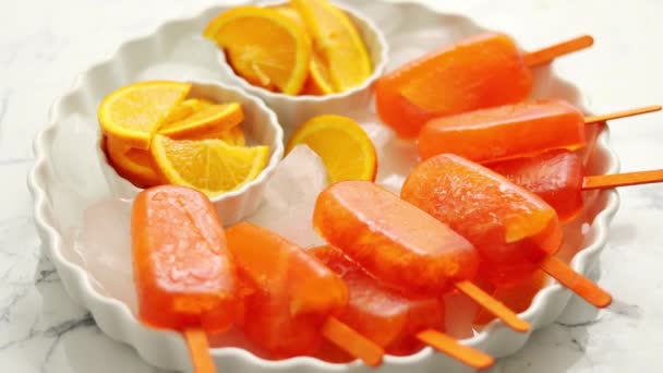 Homemade, juicy, orange popsicles. Placed on a white plate with ice cubes — Stock Video