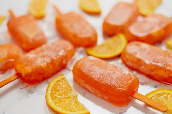 Homemade frozen popsicles made with oragnic fresh oranges placed with ice cubes on marble table — Stock Photo, Image