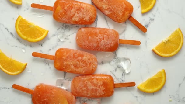 Homemade frozen popsicles made with oragnic fresh oranges placed with ice cubes on marble table — Stock Video