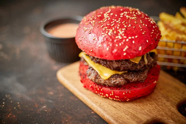 Hausgemachte rote Sesambrötchen mit doppeltem Speck-Käse-Burger. Serviert mit Pommes auf Holzbrett. — Stockfoto