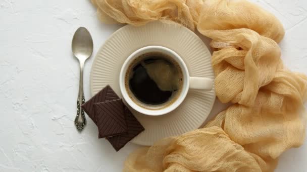 Schwarze Kaffeetasse mit dunkler Schokolade auf der Seite. Auf weißem Küchentisch — Stockvideo