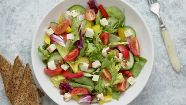 Ensalada de verduras frescas coloridas con queso feta en un tazón profundo blanco primer plano en una mesa de piedra — Vídeos de Stock