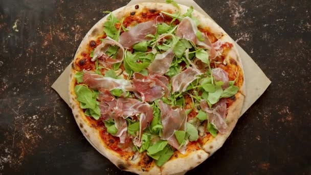 Heerlijke Pizza met prosciutto parma ham, arugula salade raket op roestig donker — Stockvideo