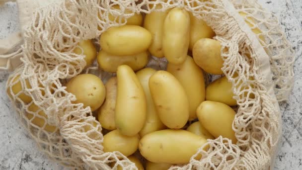 Junge frische Kartoffeln in einer ökologischen Null-Müll-Netztüte auf weißem, zerkratztem Hintergrund — Stockvideo